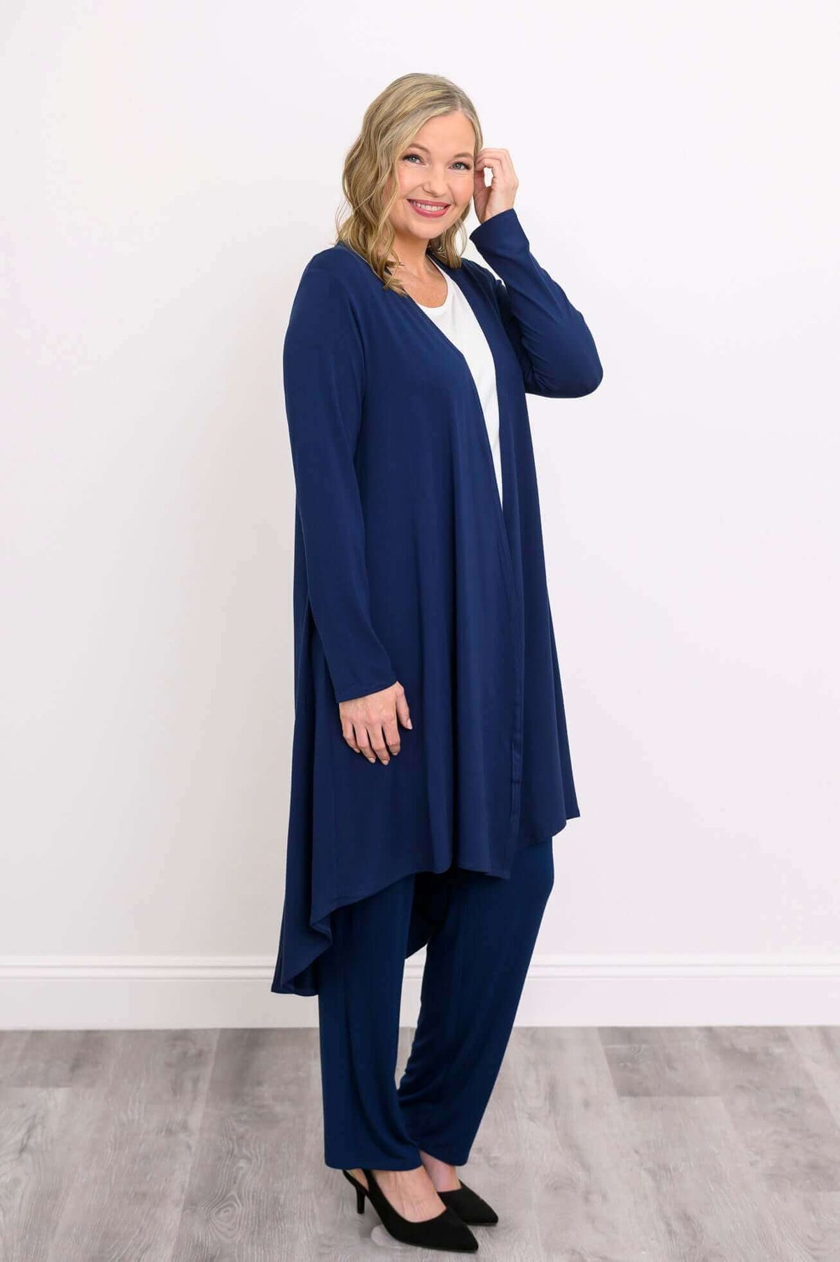 Woman posing sideways in navy blue duster cardigan with matching trousers and black shoes