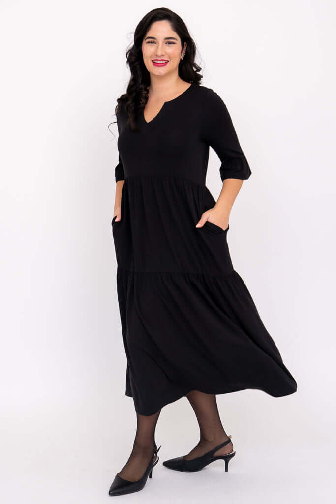Woman in black midi dress showing side view with hands in pockets