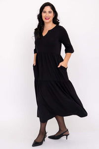 Woman in black midi dress showing side view with hands in pockets