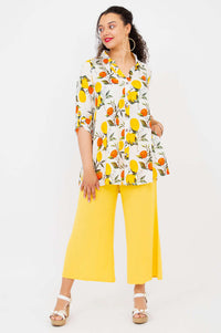Model in a citrus print tunic with hands in pockets, wearing bright yellow pants, side view