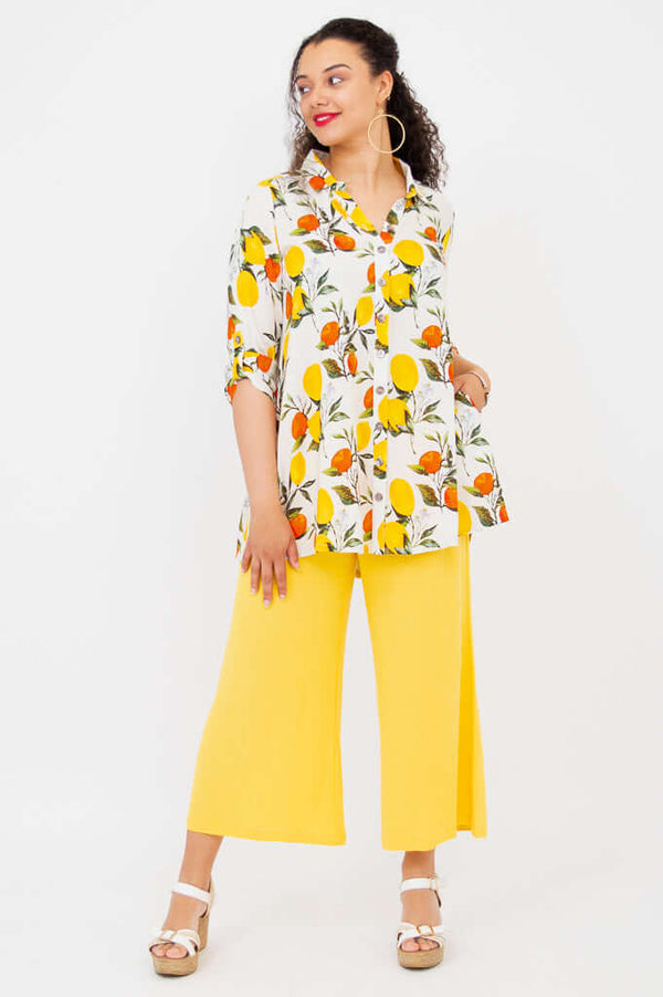 Model in a citrus print tunic with hands in pockets, wearing bright yellow pants, side view