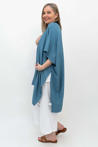 Woman showing side view of an ocean blue Darcy kimono wrap over white outfit