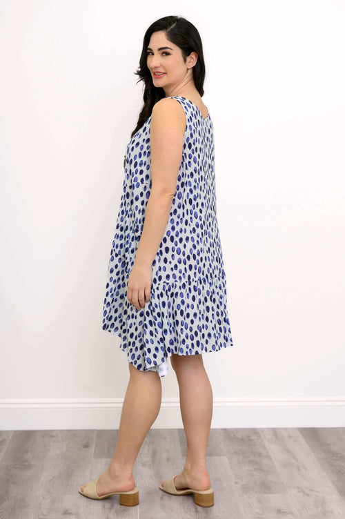 Side view of woman in blue polka dot sleeveless dress with uneven hem
