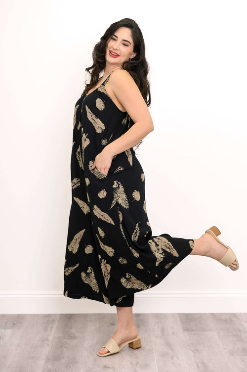 Woman in a black feather print jumpsuit, standing sideways and lifting one leg playfully