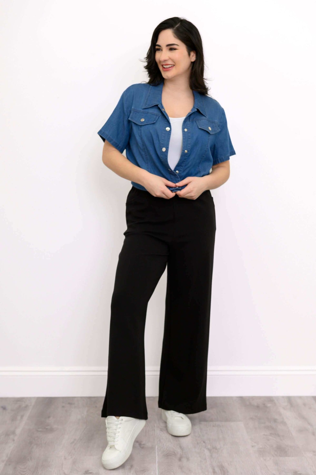 Model in blue denim jacket, white top, and black pants facing slightly to the side