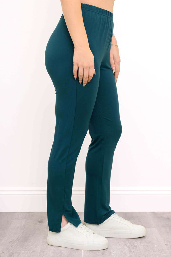 Side view of a woman wearing teal bamboo French terry slim pants showing ankle slit detail and sneakers.