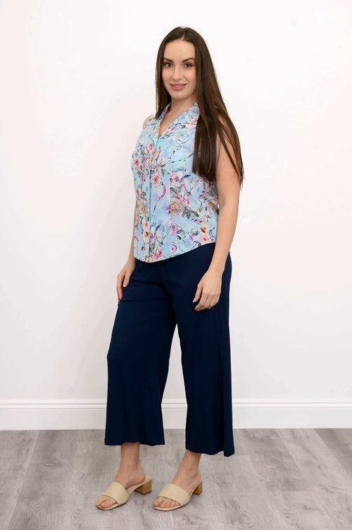 Woman posing in a light blue floral sleeveless shirt and navy pants, side view