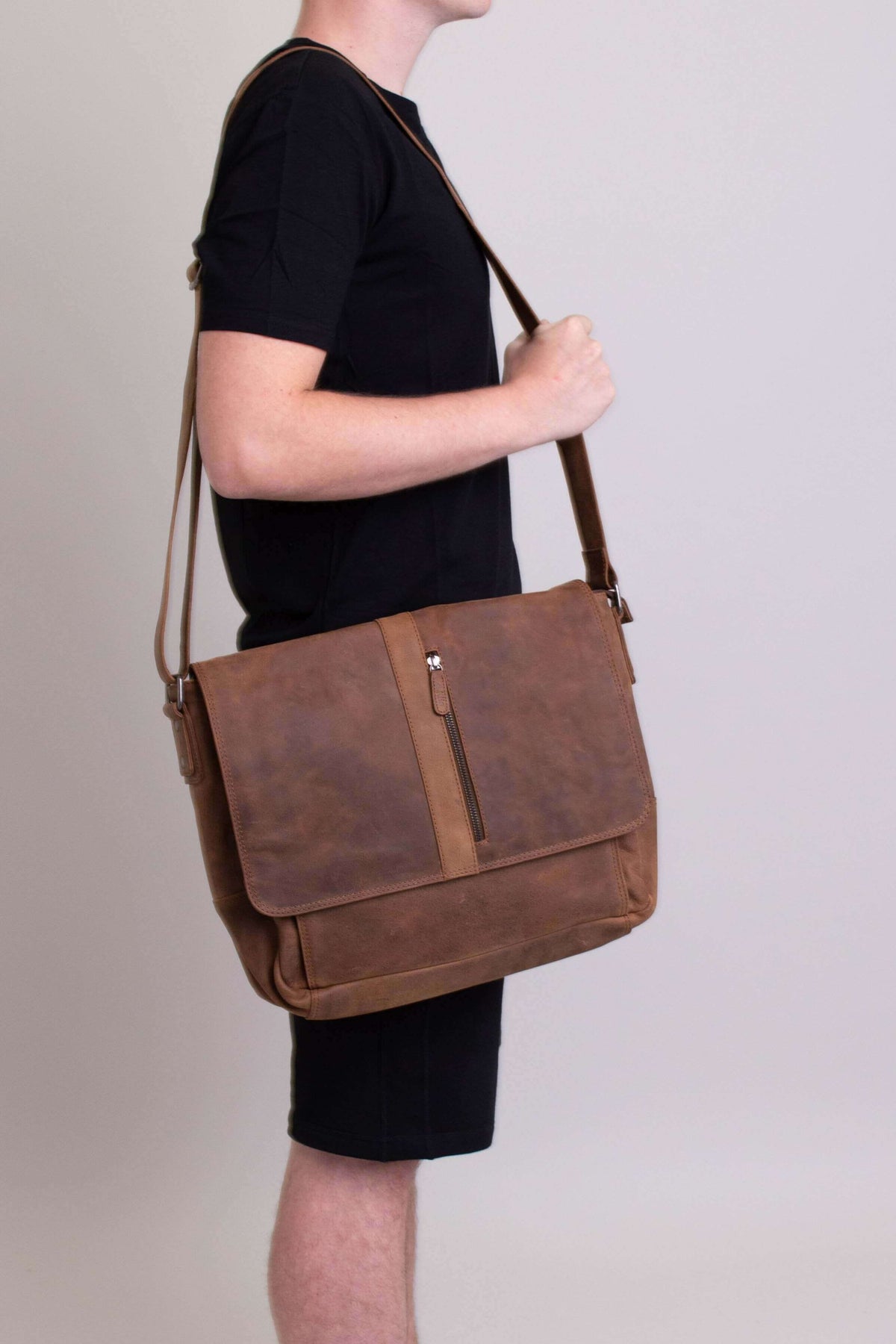 Man wearing a brown buffalo leather messenger bag with an adjustable strap, side view