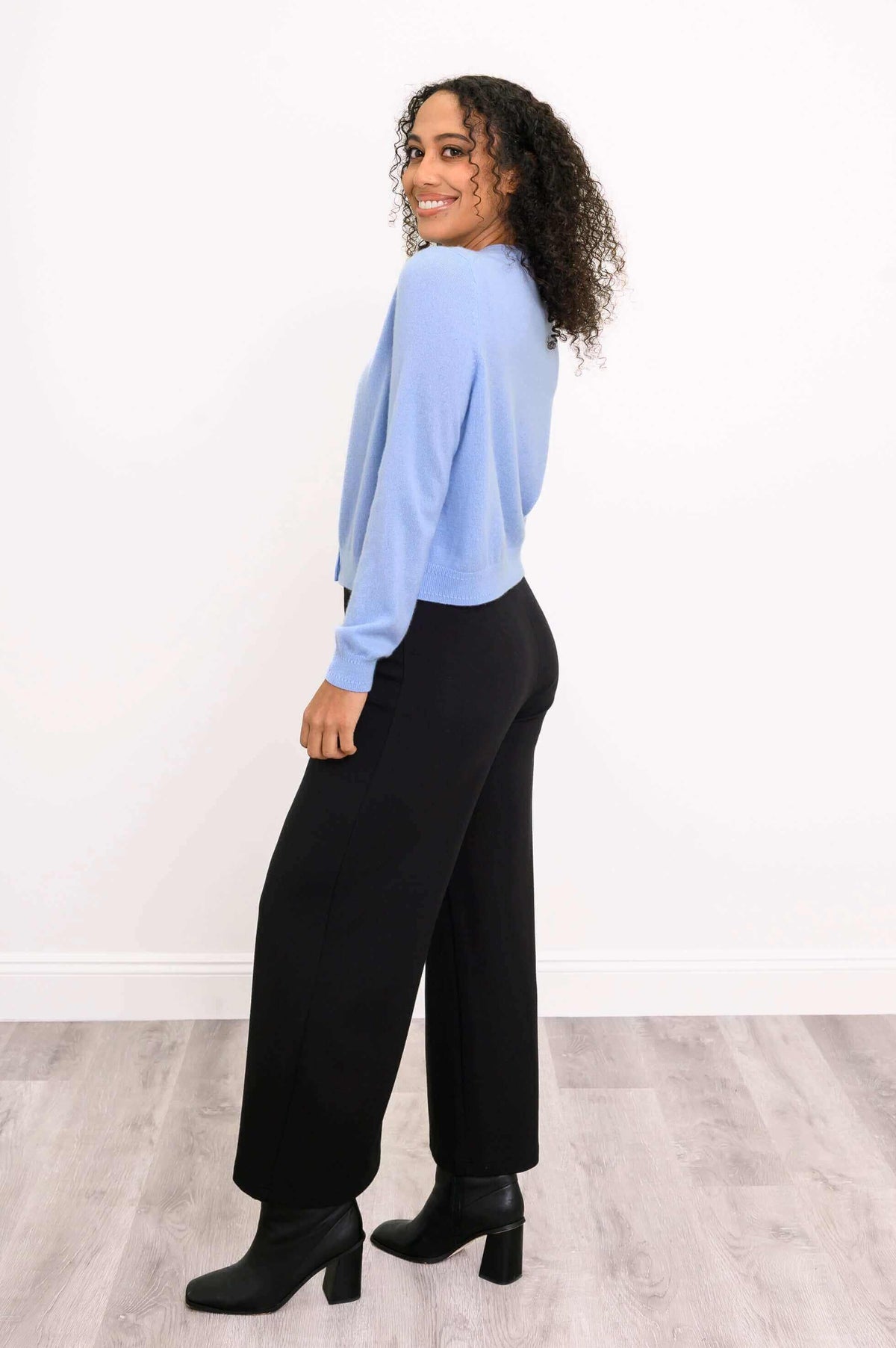 Side view of model in blue cashmere cardigan and black wide-leg trousers