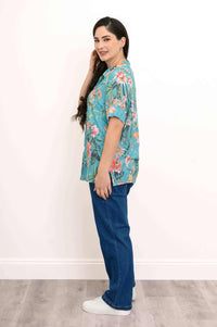 Side view of model in turquoise floral button-up blouse with rolled sleeves