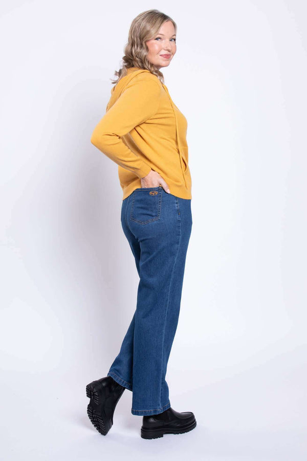 Side view of model in wide leg blue jeans and yellow hoodie, hands in pockets