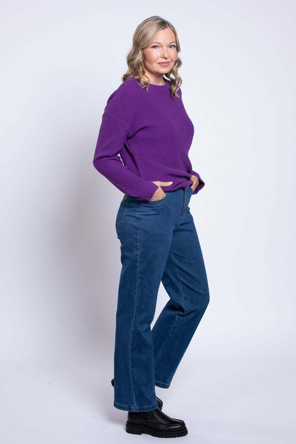 Side view of model in wide leg blue jeans with purple sweater, hands in pockets