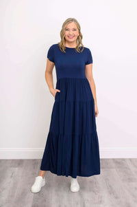 Woman in navy blue maxi dress, hand in pocket, standing on wooden floor