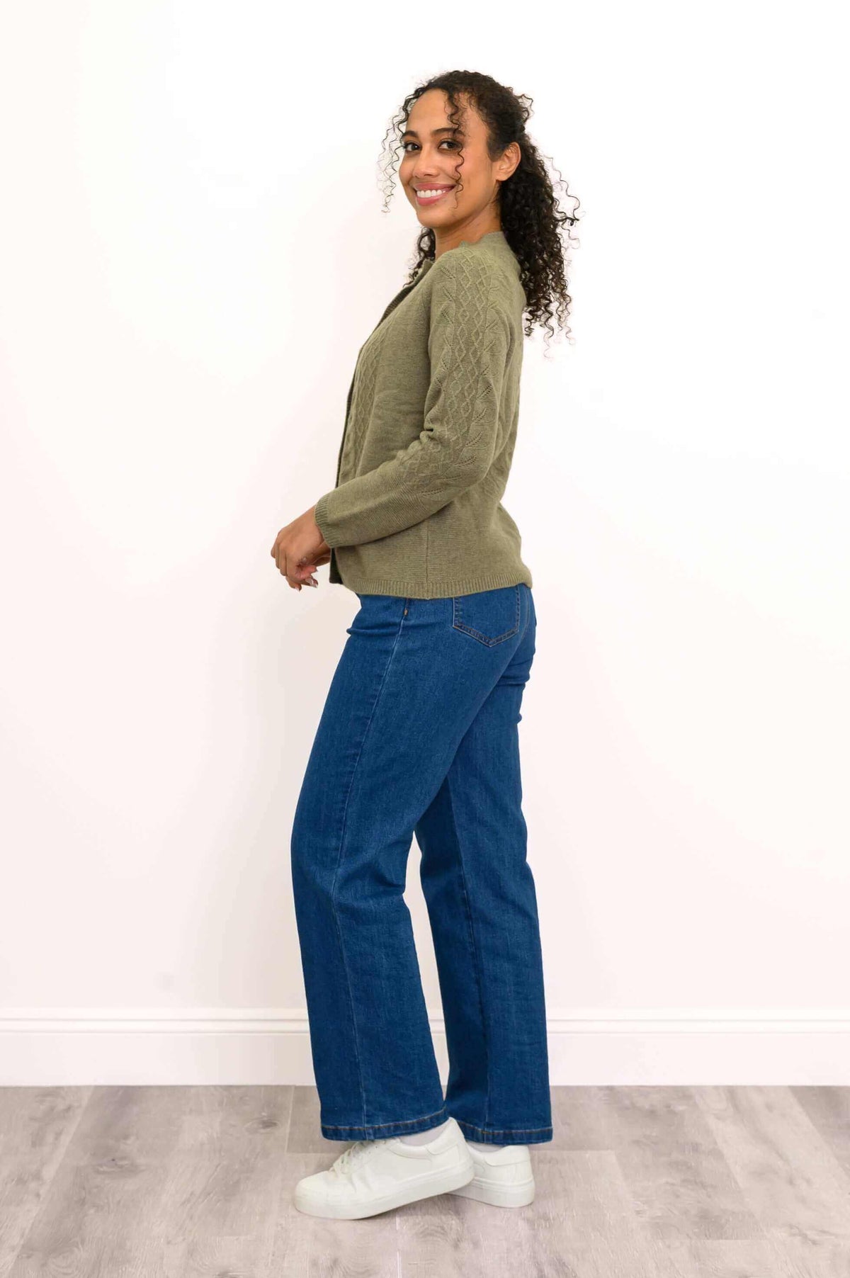 Side profile of a woman wearing an olive green cable knit cardigan and blue jeans