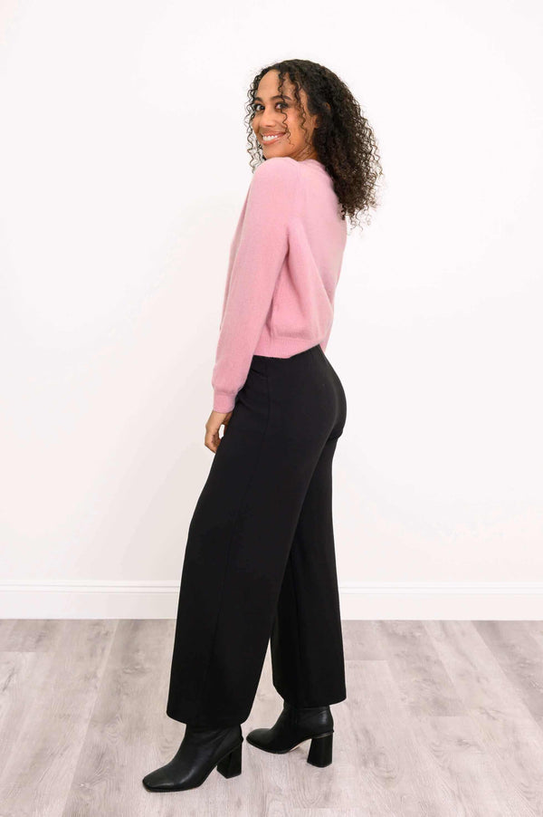 Side view of a woman in a pink cardigan and black wide-leg pants