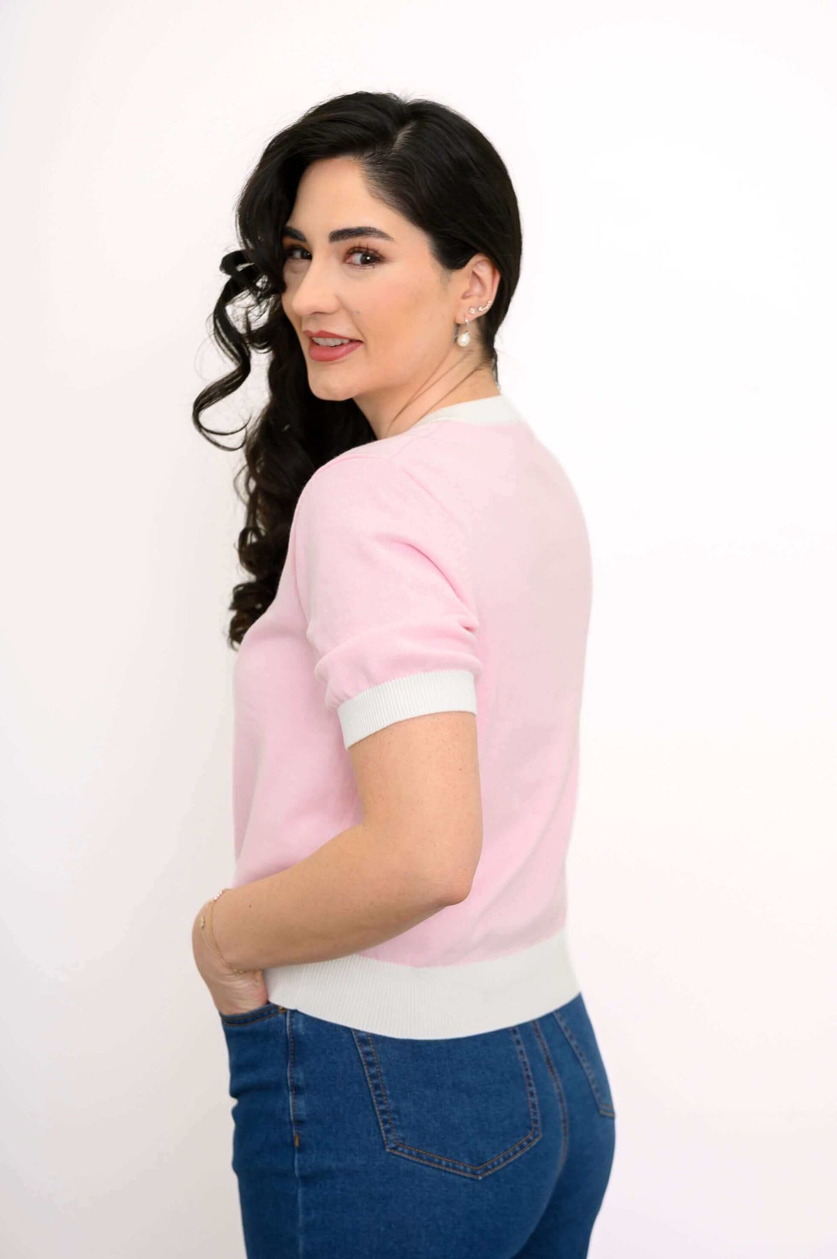 Side view of a model in a pink and white sweater with ribbed details and blue jeans