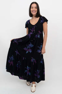 Woman displaying side of black tiered maxi dress with short flutter sleeves and fun print