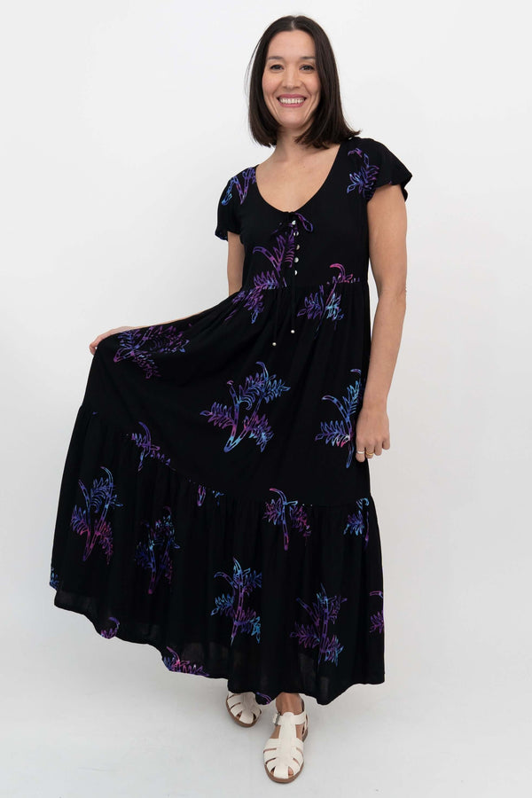 Woman displaying side of black tiered maxi dress with short flutter sleeves and fun print