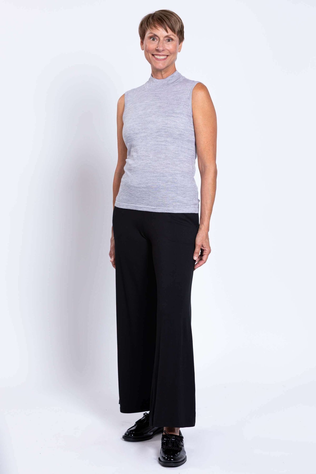 Side view of a woman in a sleeveless light grey Merino wool sweater and black pants