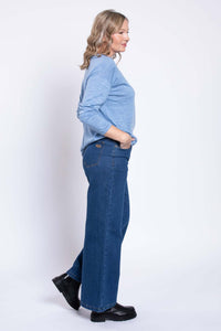 Side view of model in wide-leg blue denim jeans, light blue top, and black boots
