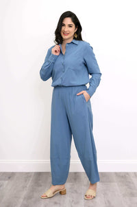 Woman in blue shirt tucked into wide-leg pants, hand in pocket, posing confidently