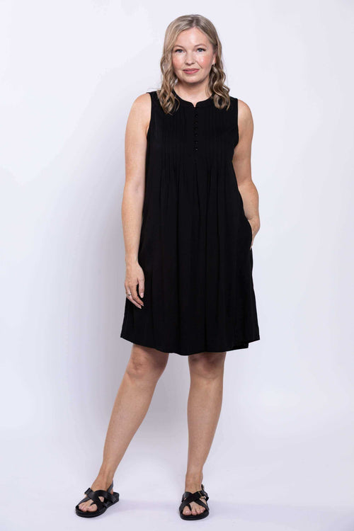 Woman in sleeveless black A-line dress with hands in pockets, front view