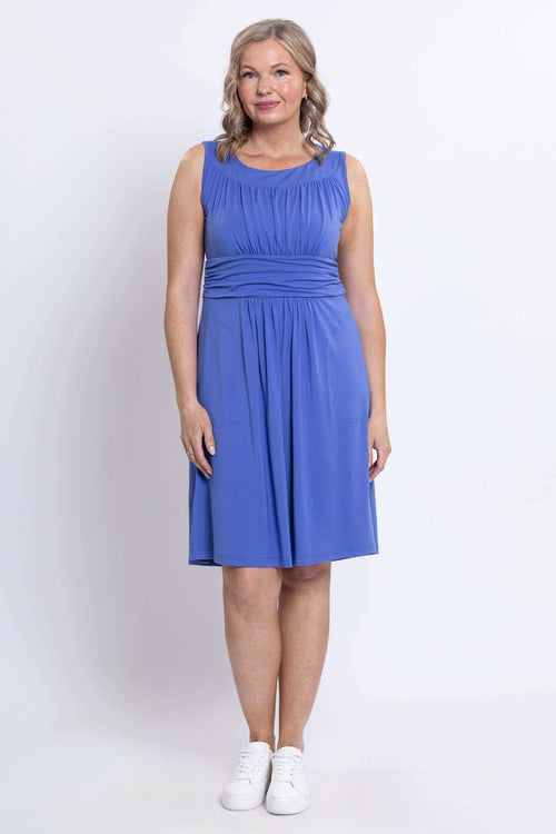 Woman wearing sleeveless blue knee-length dress with ruched bodice, front view