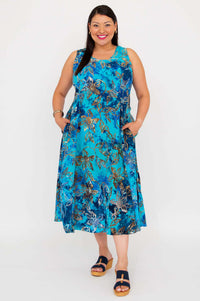Model wearing a sleeveless blue floral A-line midi dress with hands in pockets