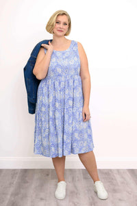 Woman wearing a sleeveless blue floral dress holding a denim jacket over her shoulder