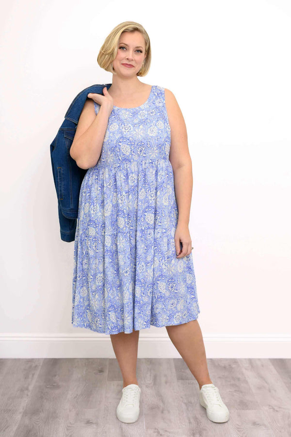 Woman wearing a sleeveless blue floral dress holding a denim jacket over her shoulder