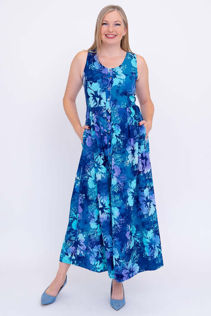 Woman wearing a sleeveless blue floral maxi dress with pockets, standing and smiling