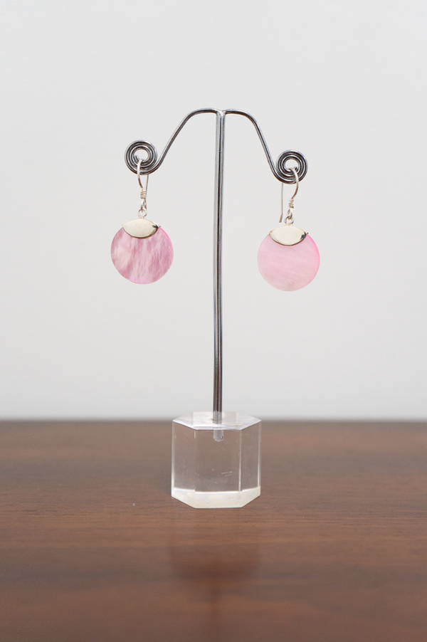 A pair on sterling silver earrings with pink shell pendants on a metal display