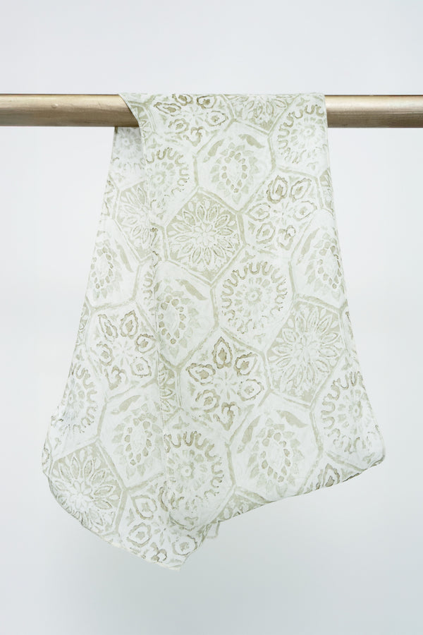 A large silk scarf with a beige geometric mosaic pattern displayed on a rod against a white background, front view