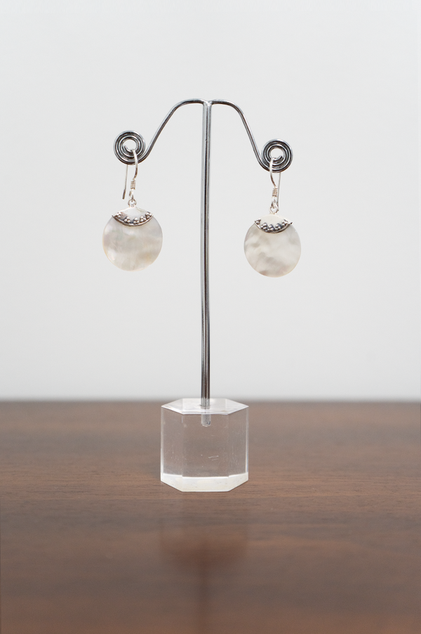 A pair of sterling silver earrings with a flat round pearl pendant displayed on a metal stand