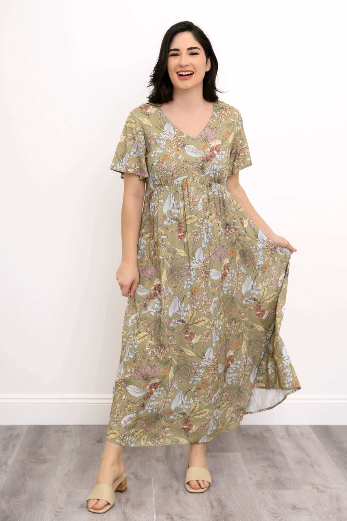 Woman smiling and holding the skirt of green floral Jane maxi dress