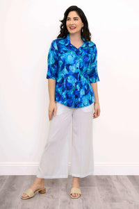 Model smiling in Lorine blue blouse and white pants, hands at side