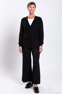 Woman smiling, standing in black cable knit cardigan and black pants