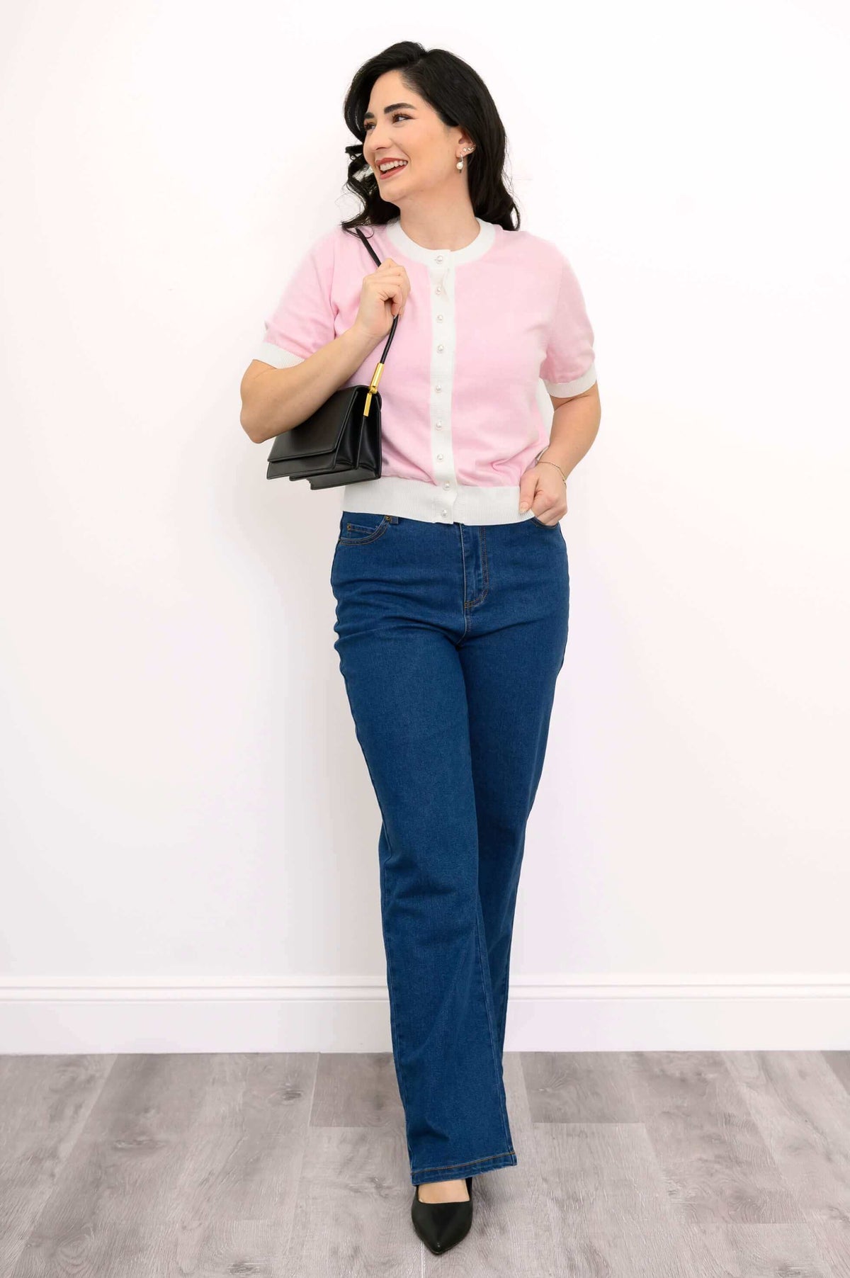 Model smiling and holding a black handbag while wearing the two-tone pink sweater and blue jeans