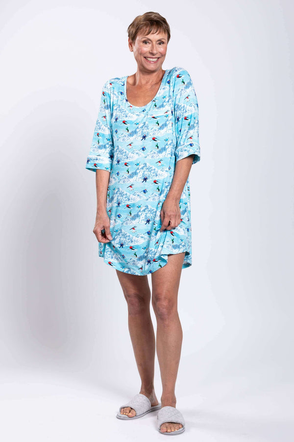 Woman in a blue sleepshirt with ski and mountain pattern, smiling, full body front view