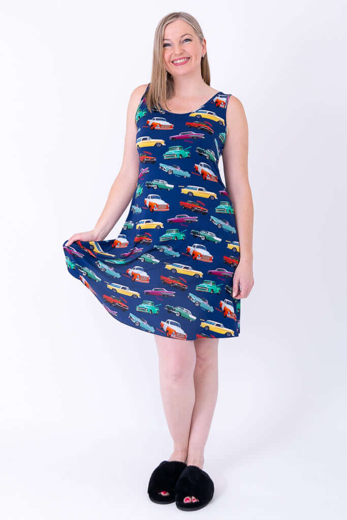 Woman smiling in sleeveless classic car print dress, holding out skirt