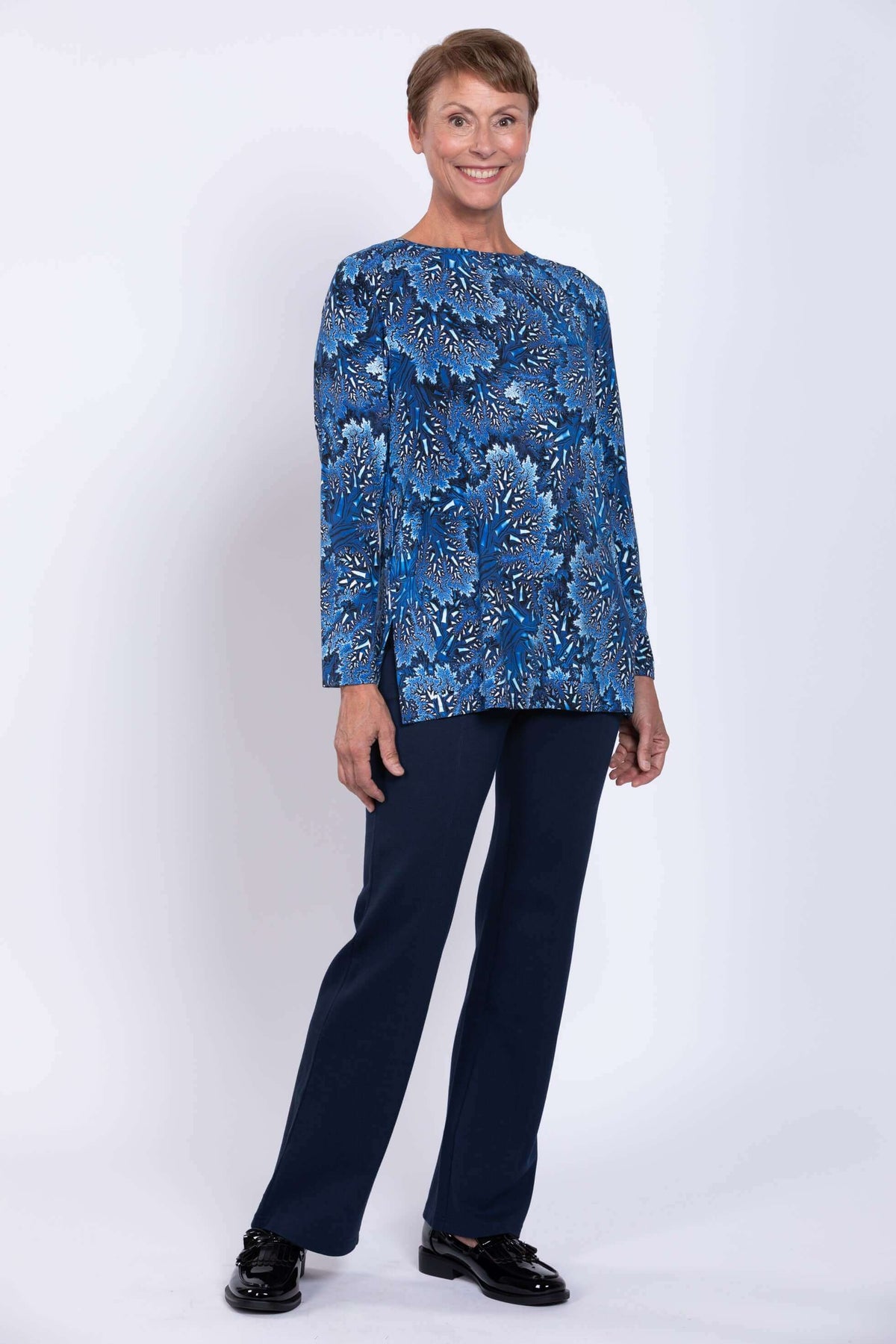 Smiling woman in blue botanical top and navy pants, angled view