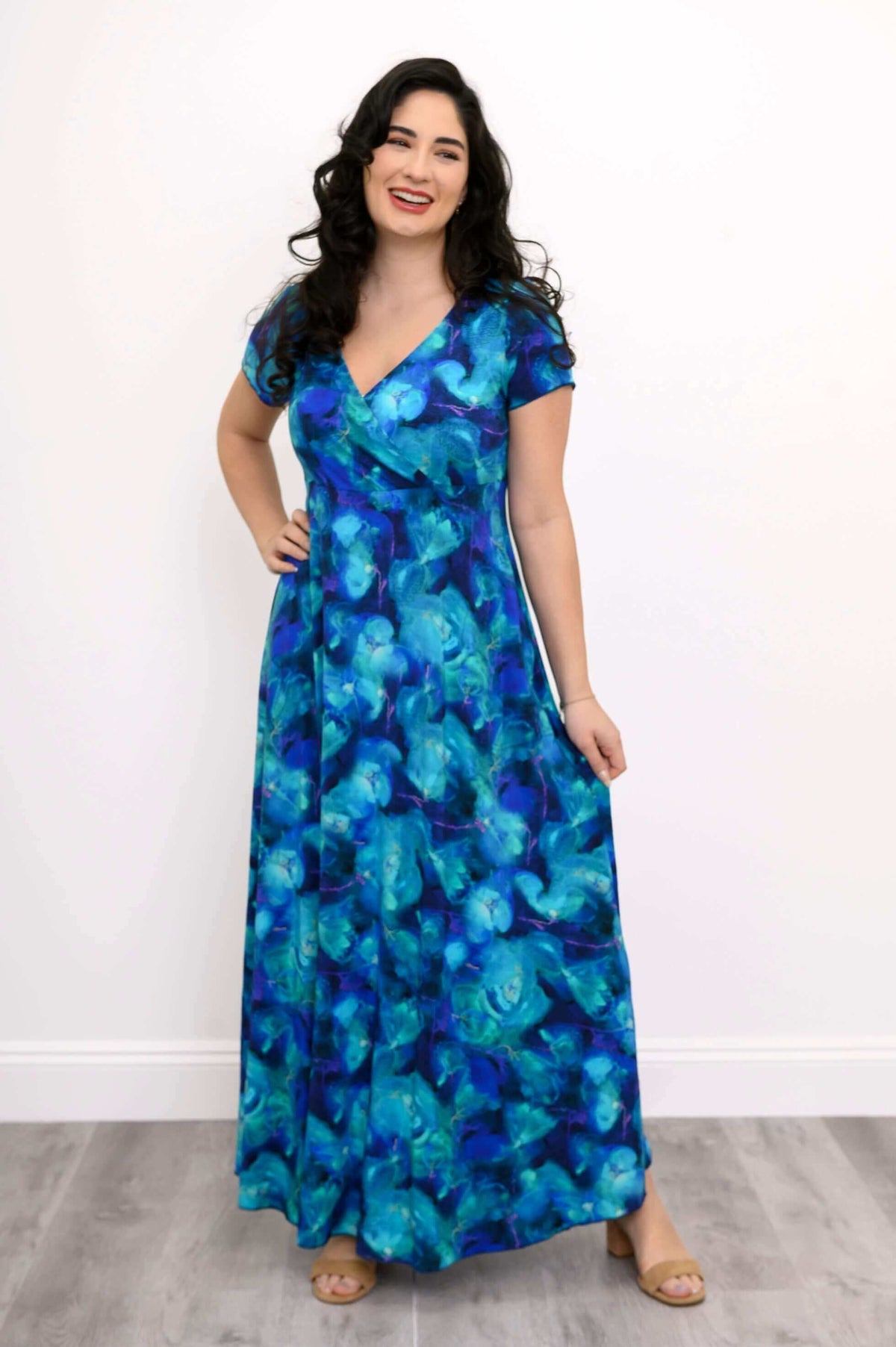 Woman in a vibrant blue and teal floral maxi dress, posing with a smile