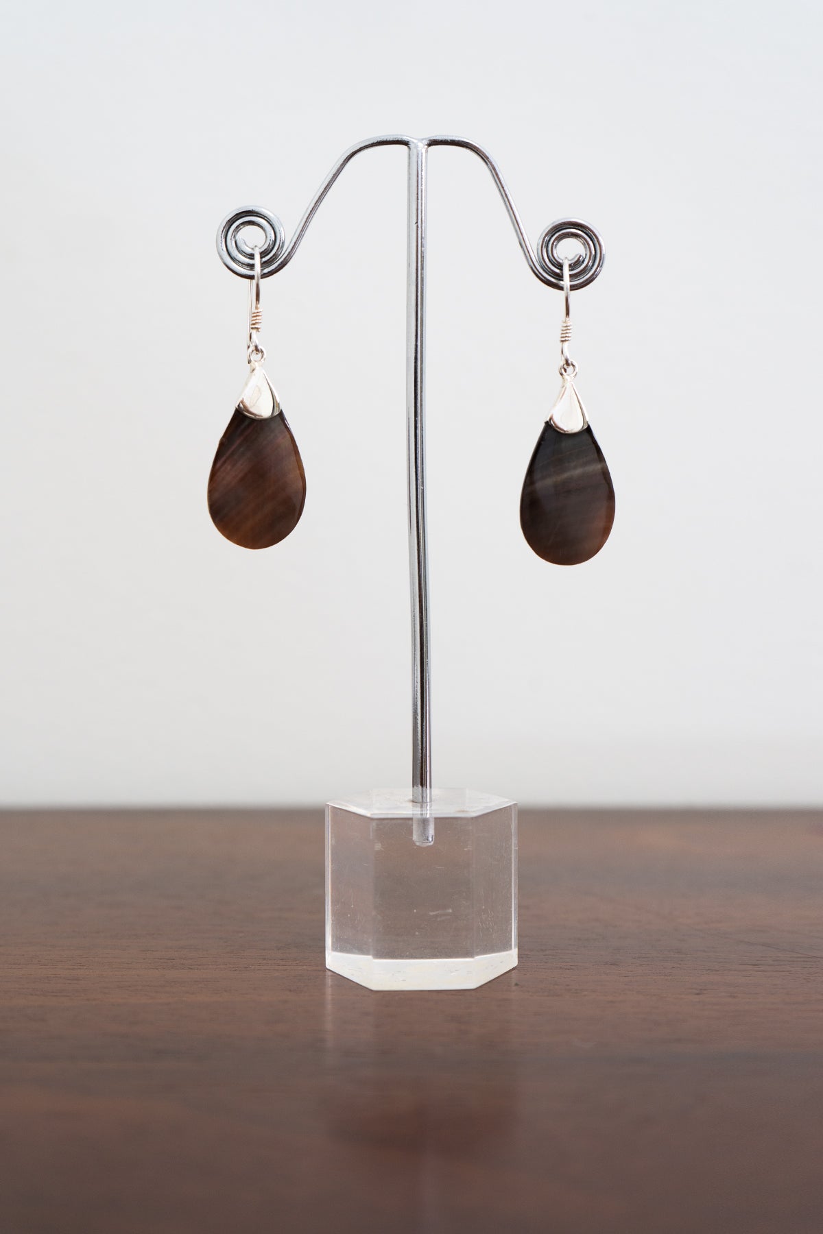Front view of a pair of sterling silver and brown stone earrings displayed on a clear stand and white background, front view