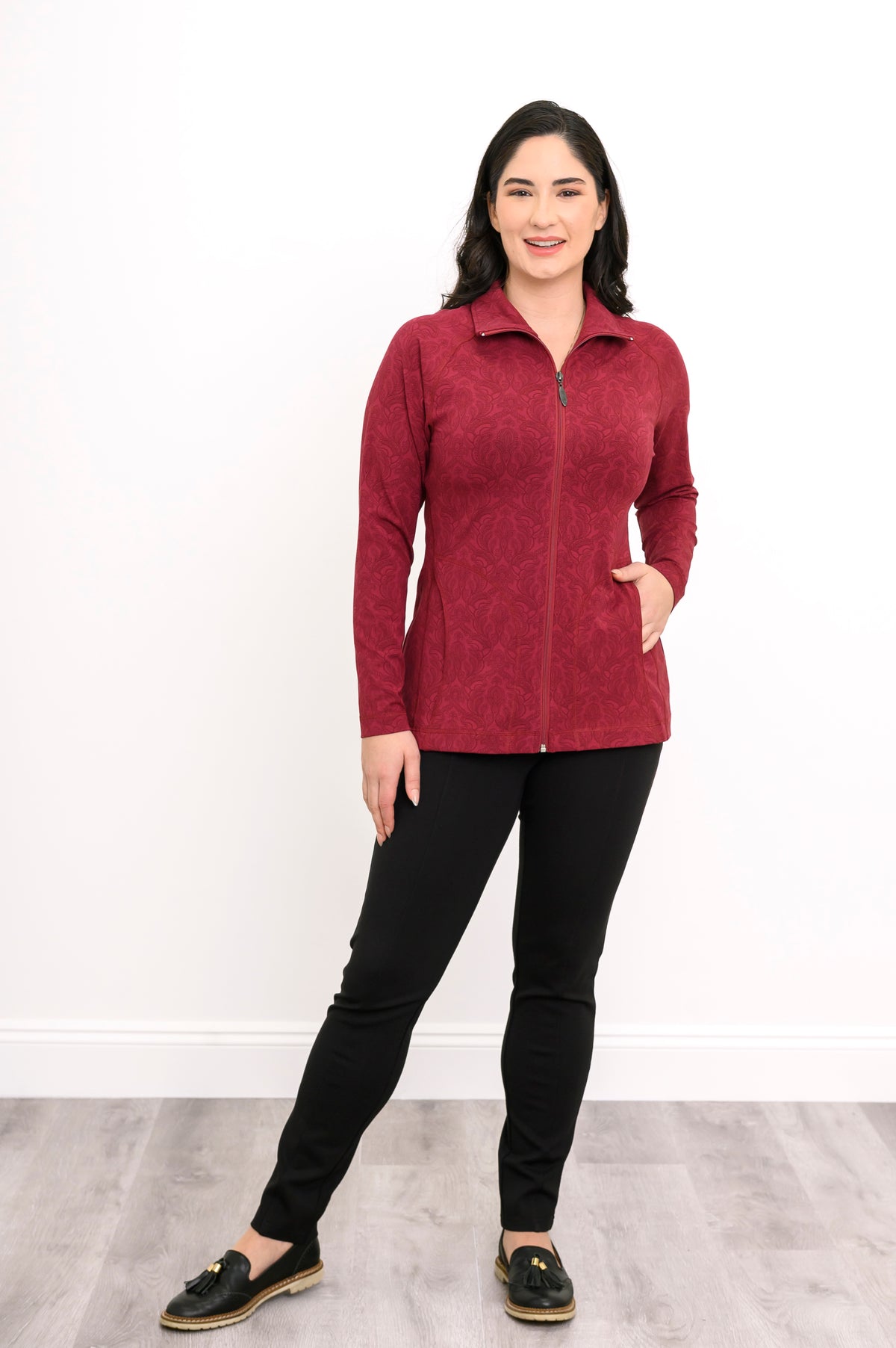 Smiling woman posing in a red patterned bamboo zip-up jacket with her hand on her hip, front-facing view.