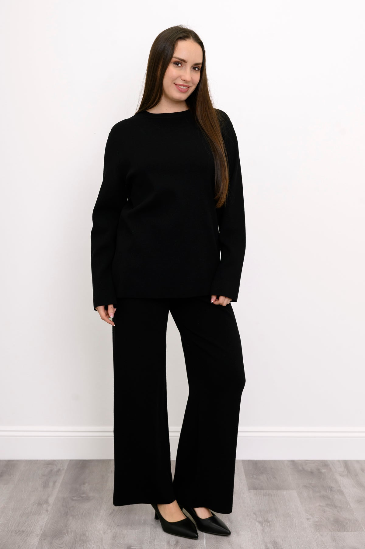 Smiling woman standing in a relaxed onyx crew neck tunic and matching knit trousers, front-facing view.