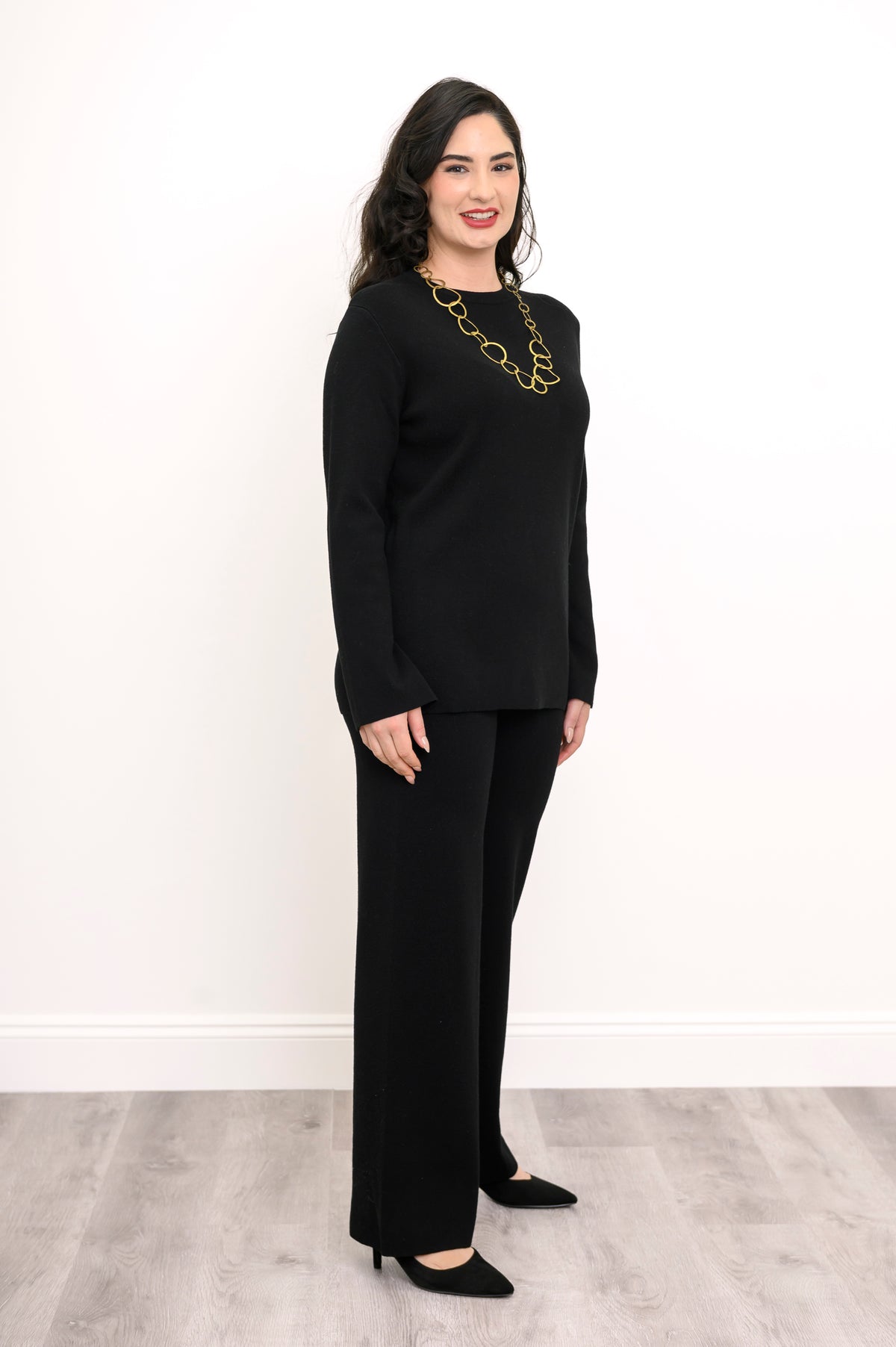 Profile shot of a women's dark charcoal sweater with long bell sleeves, styled with matching knit trousers.
