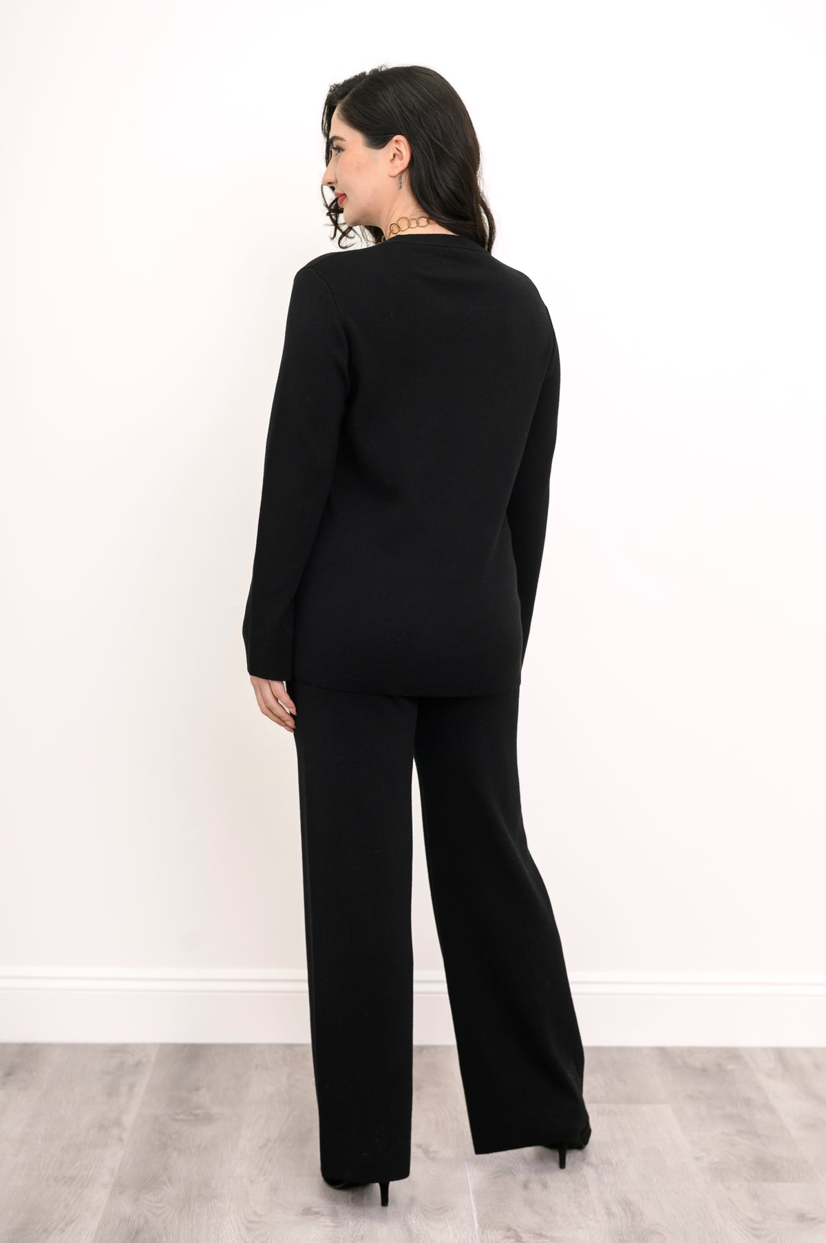 Back view of an onyx knit crew neck sweater, showcasing the clean back panel drape and flat-finish hemline.