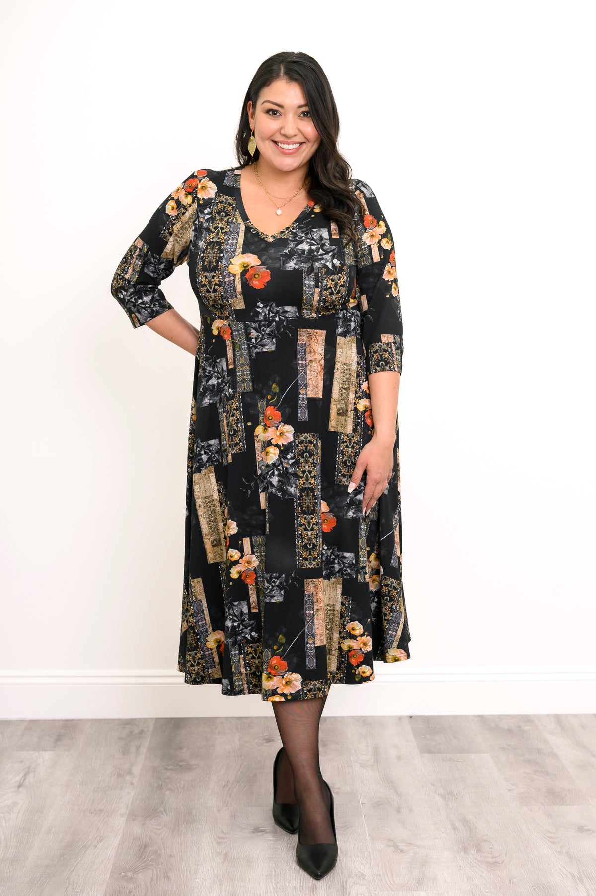 Front view of a woman modeling a black and orange floral midi dress, highlighting the flattering empire waist.