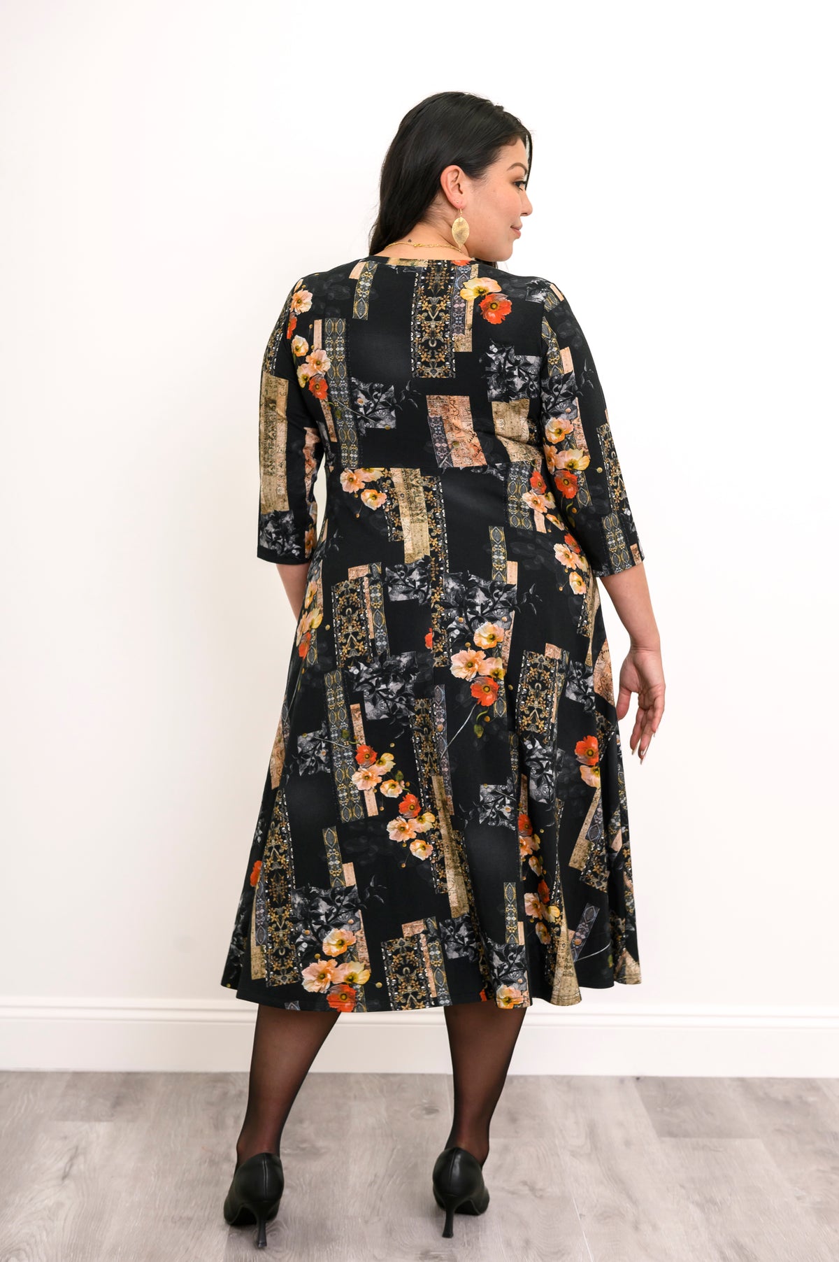 Back view of a woman wearing a black and orange floral midi dress showing the clean drape across the shoulders.