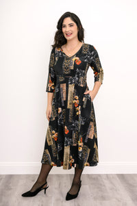 Front view of a woman modeling a black and orange floral bamboo cotton midi dress styled with simple black flats.